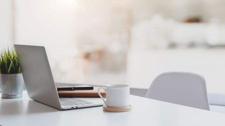 Das Bild zeigt einen Schreibtisch mit einem Laptop und einer Tasse Kaffee. Es zeigt beispielhaft einen Homeoffice Platz.